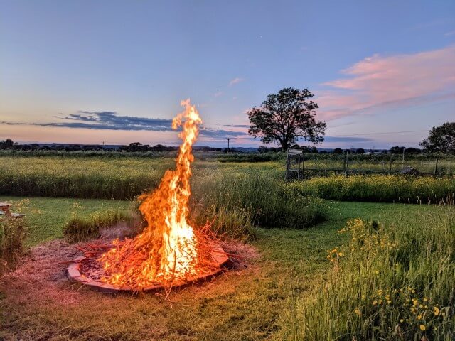 Photo of a high campfire in a field.